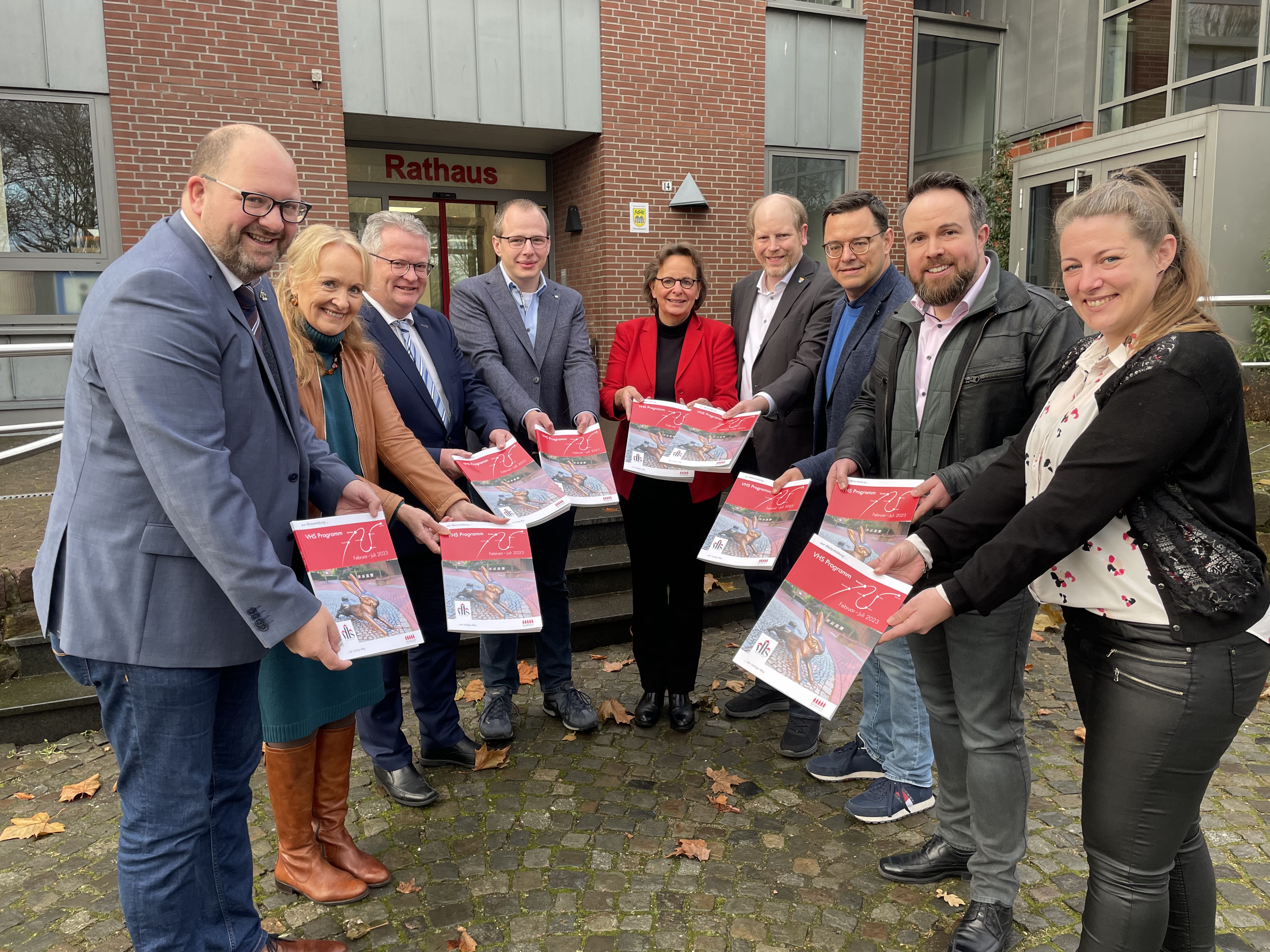 Manuel Deitert (Gemeinde Reken), Mechtild Schulze Hessing (Stadt Borken), Martin Tesing (Gemeinde Raesfeld), Benedikt Limberg (Gemeinde Heiden), Anne Kortüm (Stadt Gescher), Dr. Thomas Brüggemann (Stadt Velen), Stefan Nienhaus (Gemeinde Reken) sowie Timo Bertelwick und Nicole Brands (beide VHS) präsentieren das neue Programmheft der VHS vor dem Rekener Rathaus.